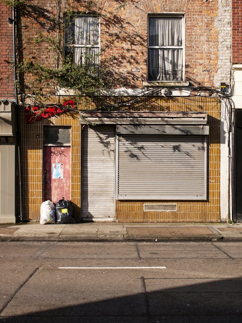 The exterior facade of Shoreditch Balls, a commercial building with a dark brick ground floor and large rectangular glass windows featuring circular signs that advertise sales and events. The windows